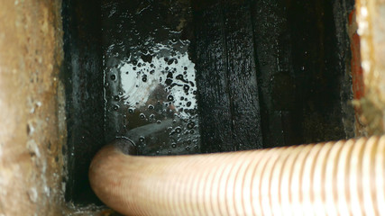 Septic cesspool emptying pumping into pipe tank by suction hose under high pressure. The sump contains pollution sludge sewage water black wastewater and faeces plus excrements from home