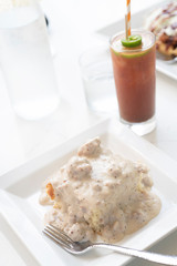 Brunch scene with biscuits and gravy on a white plate with a bloody mary