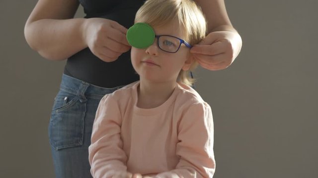 Portrait of funny child in new glasses with green spot to correct strabismus Orthopedic Boys Eye Patches nozzle for glasses for treatment of strabismus (lazy eye). Boy puts on and corrects glasses