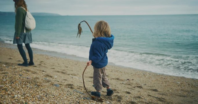 Toddler walking on the beach with his mother on a winter day