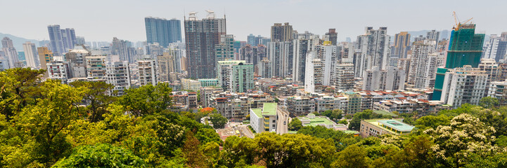 Fototapeta na wymiar MACAO, CHINA - May 28, 2017: View of Macao skyline with residential / apartment buidlings. In the foreground green trees of Guia Park. Urban panorama of an asian city. 3:1 format.