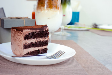 piece of chocolate cake and fork in the dish on the table near gift box on the table.