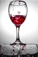 Stream of red wine falling into a transparent glass with splashes