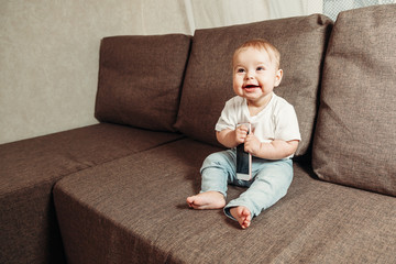 A small child behaves like an adult. Independence, modern children's toys. Little smiling child sitting on the sofa bed with the phone in hand