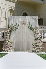 The square arch is decorated with elegant chandelier, white veil and large compositions of fresh flowers on the sides