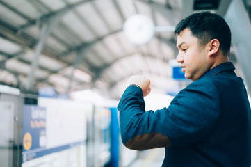 Asian businessman looking at his watch, waiting train platform