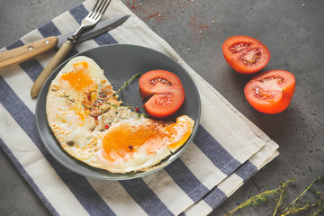 scrambled eggs with tomato, thyme, pepper and sesame on a plate on a gray background, fork, knife, healthy