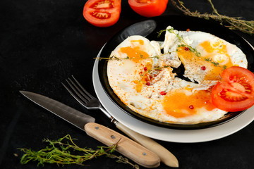 scrambled eggs with thyme and tomato on a plate on a black background, knife, fork, Breakfast,