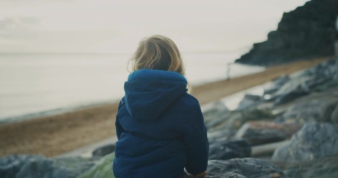 Little toddler climbing on rocks by the sea