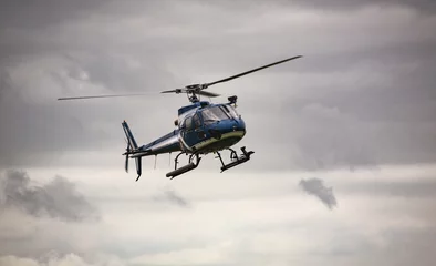 Fotobehang Helikopter Blauwe helikopter tijdens de vlucht over grijze lucht