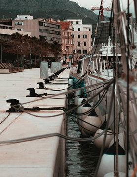 Boats and sailbots docked in a long marble harbour of split,croatia. Side view paralel with houses and a mountain in the background