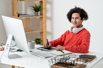 Successful young freelancer with stylus retouching photos in graphics tablet