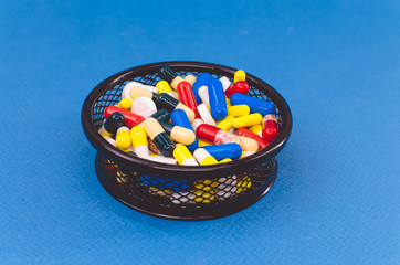 pile of pills of different colors in a black basket against a blue background