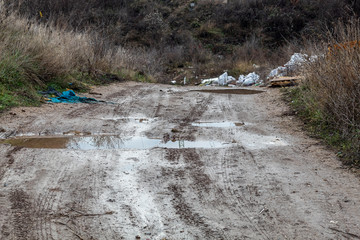 Dirt Road With Puddles and Garbage Thrown in Wrong Place