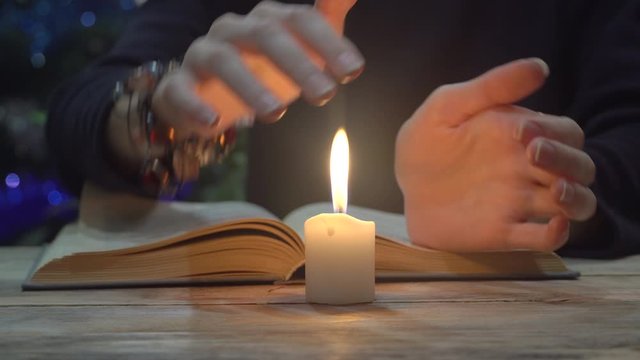 close-up. a fortuneteller reads an old book, casts spells, amid darkness, darkness and burning candles. cards on the table.