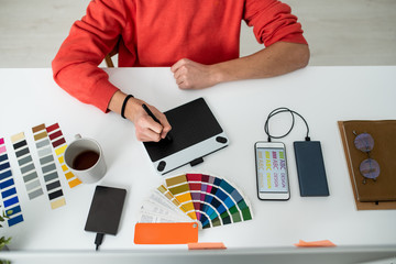 Hands of young male web designer with stylus during retouching work by desk