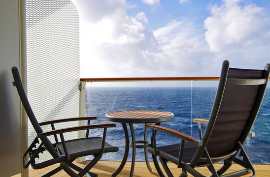 Deck chairs or sun loungers with table on balcony or terrace or patio of luxury cabin stateroom suite on modern cruise ship liner with amazing oceanview