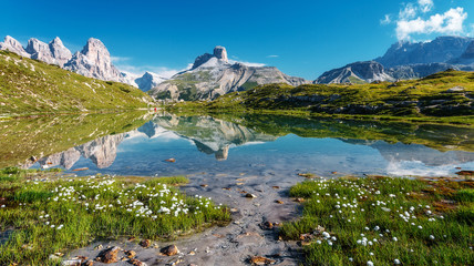 Amazing Nature Landscape. Alpine lake with crystal clear water and frash grass and flowers. Perfect Blue sky and mountains peaks. Incredible view of Dolomites Alps. Tre Cime di Lavaredo National park.