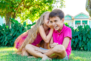 Little girl whispering a joke in a boy's ear, boy is laughing, summer garden background