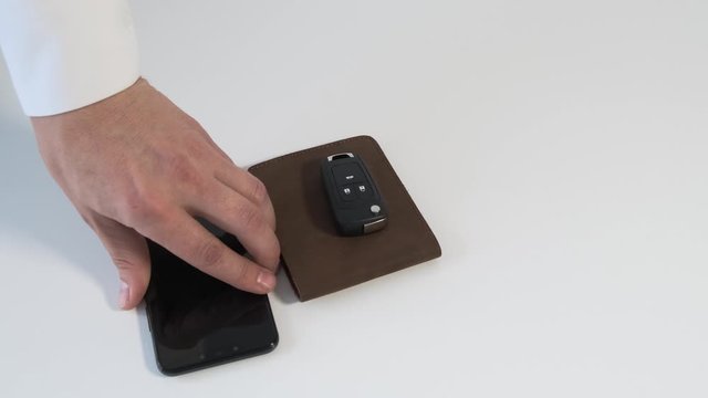 Hand putting car key , wallet, smartphone on white table. Close up.