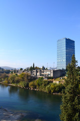 Fototapeta na wymiar Skyscraper watching on blue clear river. Green cypress.Podgorica. Montenegro