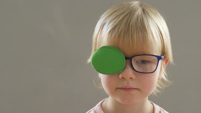 Portrait of funny child in new glasses with green spot to correct strabismus Orthopedic Boys Eye Patches nozzle for glasses for treatment of strabismus (lazy eye). Boy puts on and corrects glasses