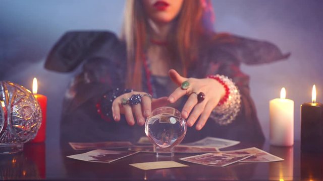 Witch making potion by telling occult spell and moving crystal ball, evil concept. Magic gypsy calling spirits of dead people in dark room, fear in the air, paranormal demon's rituals, evil and good