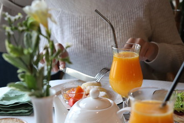 Breakfast in the cafe. Girl holds a fork and knife eating cheesecakes with berries. Fresh orange juice and coffee on the table.