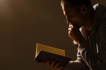 Man praying to God with his hands resting on a bible.