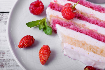 Piece of cake with many layers topped with fresh berries and mint on a ceramic plate
