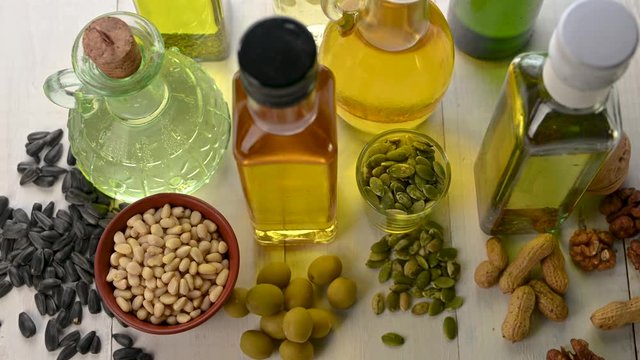 several bottles of different oil stand on a wooden table with nuts