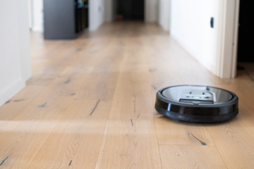 robot vacuum cleaner that moves independently on a house with wooden parquet. Round robot vacuum...