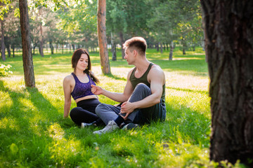 A young, athletic couple, a guy and a girl are sitting nearby in a park on a lawn.