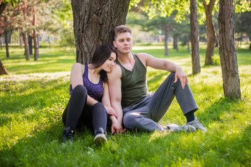 Naklejka na ściany i meble Athletic guy and girl sitting on the lawn leaning against a tree.