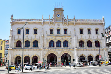 Naklejka na ściany i meble Lisbon, Portugal - Rocio Station (Rossio Train Station), a beautiful white building with horseshoe-shaped doors and a clock at the top, a street with cars and people in the summer afternoon.