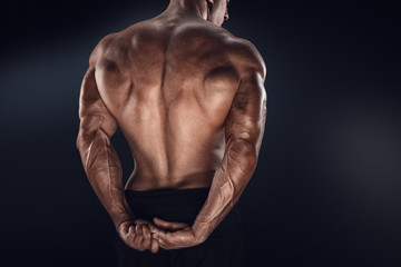 Close-up of handsome power athletic man showing his back. Strong bodybuilder with shoulders, biceps, triceps and chest Fitness muscular body on dark background. Fitness sports.