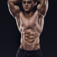 Sexy shirtless male model young bodybuilder posing over black background. Studio shot on black...