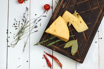 Masdam cheese on a dark board next to sprigs of lavender on a white wooden table