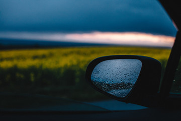 view on blurred flower field and mirror in drops from the car window