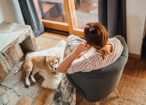 Young female sitting in comfortable chair in country house  living room and dreaming and her beagle dog lying near feet on the natural sheepskin. Home sweet home concept image.