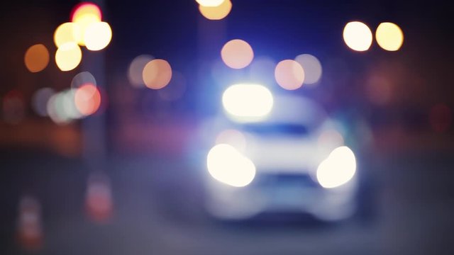 Unfocused shot, front view of police car and officer at night. Road traffic accident concept. Street lamp lights bokeh.