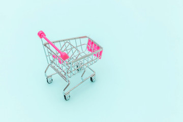 Small supermarket grocery push cart for shopping toy with wheels isolated on blue pastel colorful trendy background Copy space. Sale buy mall market shop consumer concept.