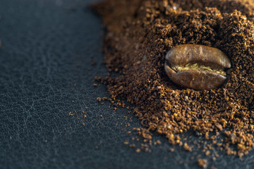 Fototapeta na wymiar Coffee bean lies on ground coffee. Conceptual photo. Close-up on a black texture background.