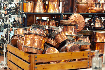 Old cleaned copper utensils piled in a wooden box in a store.