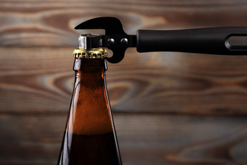 A bottle of beer, made of dark glass with a golden cork, opens with a black opener for beer, on a...