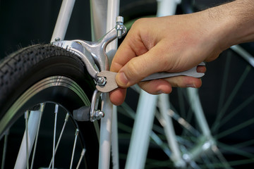 Bicycle repair. Restoration of a very old road racing bike. Rear V-brake and tire closeup. White frame. The mechanic holds a spanner in his hand. Black background.