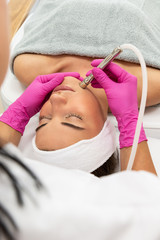 Kosmetolog wykonuje zabieg mikrodermabrazji skóry twarzy kobiety w salonie kosmetycznym. Kosmetologia i profesjonalna pielęgnacja skóry.