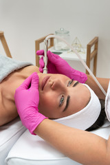 Kosmetolog wykonuje zabieg mikrodermabrazji skóry twarzy kobiety w salonie kosmetycznym. Kosmetologia i profesjonalna pielęgnacja skóry. - obrazy, fototapety, plakaty