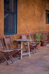 Rustic wooden outdoor chairs and a table against orange wall