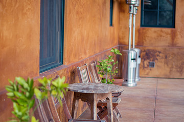Rustic wooden outdoor chairs and a table against orange wall